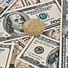 A golden Bitcoin rests on a scattered pile of United States hundred-dollar bills.