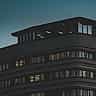 A sleek modern office building with illuminated windows captured at dusk against a moody sky.