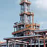 A bright daytime view of intricate pipelines and towers at a large oil refinery.