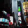 The iconic cylindrical Nasdaq MarketSite building illuminated among the vibrant billboards of Times Square in New York City.