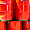 Bright red industrial oil barrels stacked outdoors in bright daylight.