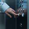 A business professional's hand pressing an illuminated button on a modern elevator control panel.