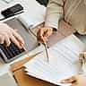 Overhead view of two people using pens to point out specific details on a printed document next to a laptop.