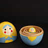 A small yellow and blue wooden nesting doll sits inside the opened base of a larger matching doll against a black background.