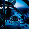 A glowing marine compass mounted on the steering binnacle of a sailboat navigating at twilight.
