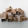 A large pile of plain, empty cardboard boxes of various sizes stacked in a bright, minimalist space.