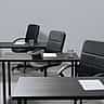 Empty black chairs and desks in a stark, desaturated corporate office setting.