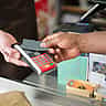 A customer taps a credit card on a payment terminal held by a service worker wearing an apron.
