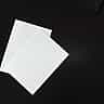 Two blank sheets of white paper lie side-by-side on a dark surface.