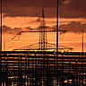 Silhouetted electrical transmission towers stand against a vibrant orange and yellow sunset.