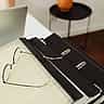 A pair of wire-rimmed reading glasses resting on a document over a black binder next to a silver laptop.