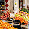 An older man looks at a display of fresh fruit at an outdoor market in Italy.