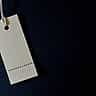 A minimalist blank white tag hangs by a string against a dark background.