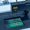 Close-up of an automated inspection machine working on a green printed circuit board in a manufacturing facility.