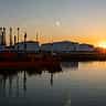 The dark silhouette of an oil tanker ship and storage tanks against a vibrant orange sky.