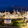 Aerial view of a sprawling oil refinery glowing brightly with complex lights against a dark night sky.