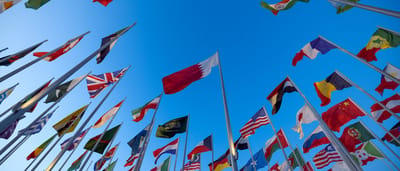 A vibrant collection of international flags from various nations waving together against a clear blue sky.