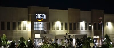 An illuminated Amazon warehouse building at night with glowing blue signage.