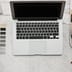 A clean, modern workspace viewed from above featuring a silver laptop, coffee, and color swatches on a white marble surface.