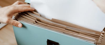 Hands placing a crisp white document into an organized blue accordion file on a wooden desk.