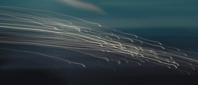 Abstract white light trails streaking upward across a dark blue background, suggesting speed and forward momentum.