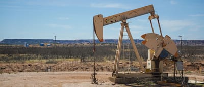 An industrial oil pumpjack operates in a desert landscape under a clear blue sky.