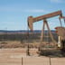 An industrial oil pumpjack operates in a desert landscape under a clear blue sky.
