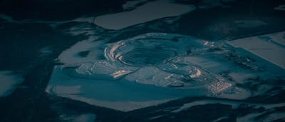 An aerial view of a massive open-pit mine covered in deep snow at twilight.