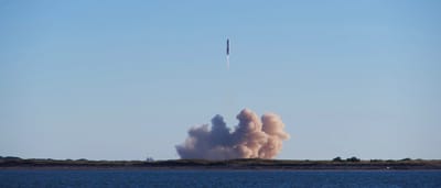 A powerful rocket launches into the sky over the ocean, leaving a thick plume of smoke in its wake.