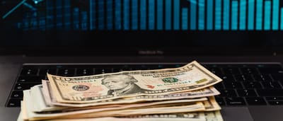 U.S. dollar bills resting on a modern laptop keyboard, symbolizing the digitization of traditional currency.