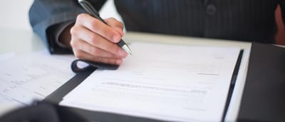A close-up of a professional in a suit signing an official document with a pen.