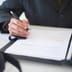 A close-up of a professional in a suit signing an official document with a pen.