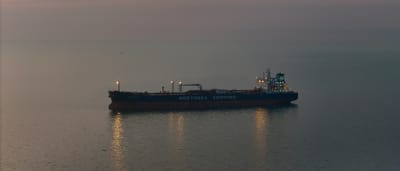 A large oil tanker sails alone across dark, open waters under a dim twilight sky.