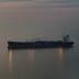 A large oil tanker sails alone across dark, open waters under a dim twilight sky.