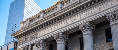 A classic stone bank facade with 'United States National Bank' engraved above sturdy columns, set against a modern glass skyscraper.
