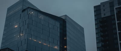 Modern glass office buildings stand under a dark, overcast evening sky.