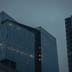 Modern glass office buildings stand under a dark, overcast evening sky.