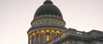 The illuminated dome of a neoclassical state capitol building stands against a darkening twilight sky.