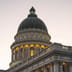 The illuminated dome of a neoclassical state capitol building stands against a darkening twilight sky.