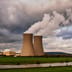 Cooling towers of a power plant emit plumes of steam under cloudy skies.