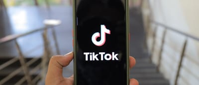 A hand holds a smartphone displaying the TikTok logo on the screen in a modern building.