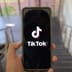 A hand holds a smartphone displaying the TikTok logo on the screen in a modern building.