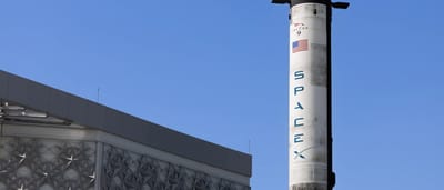 A SpaceX Falcon 9 rocket stands vertically on display against a clear blue sky.
