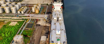 An aerial view of large industrial oil storage tanks and a docked tanker ship at a coastal facility.