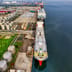 An aerial view of large industrial oil storage tanks and a docked tanker ship at a coastal facility.