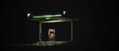 An isolated gas station glows brightly against a dark night sky.