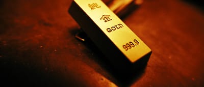 A close-up of a physical gold bar with investment-grade inscriptions under warm lighting.