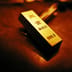 A close-up of a physical gold bar with investment-grade inscriptions under warm lighting.