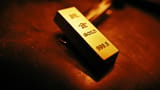 A close-up of a physical gold bar with investment-grade inscriptions under warm lighting.