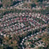An aerial view of a large suburban neighborhood with identical houses arranged in concentric circles among autumn trees.